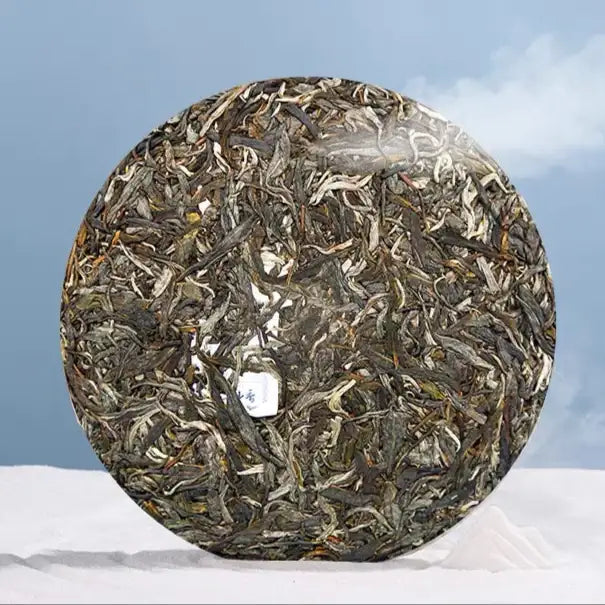 Round compressed Chinese pu-erh tea cake with visible tea leaves, displayed on a white cloth background.