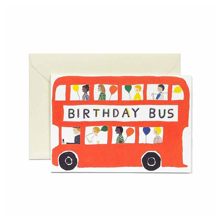 Greeting card featuring an illustration of a red bus with kids and balloons, reading “Birthday Bus,” shown with a cream envelope.