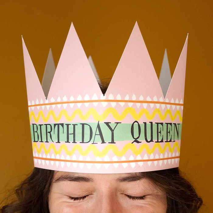 Person wearing a pink paper crown with 'Birthday Queen' text on a brown background